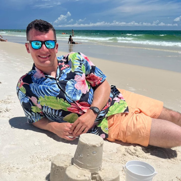 Man on a beach wearing a floral Tommy Bahama aloha shirt