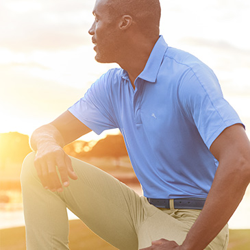 man kneeling on golf course in performance polo and pants